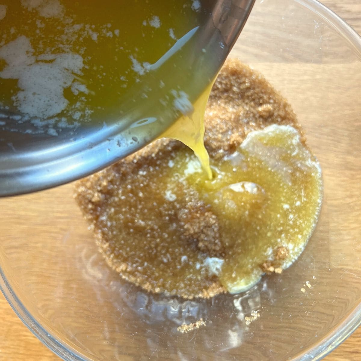 Pouring melted butter into sugar in glass bowl.