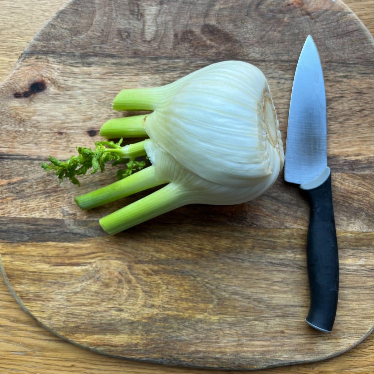 Full fennel on wooden chopping board with knife.