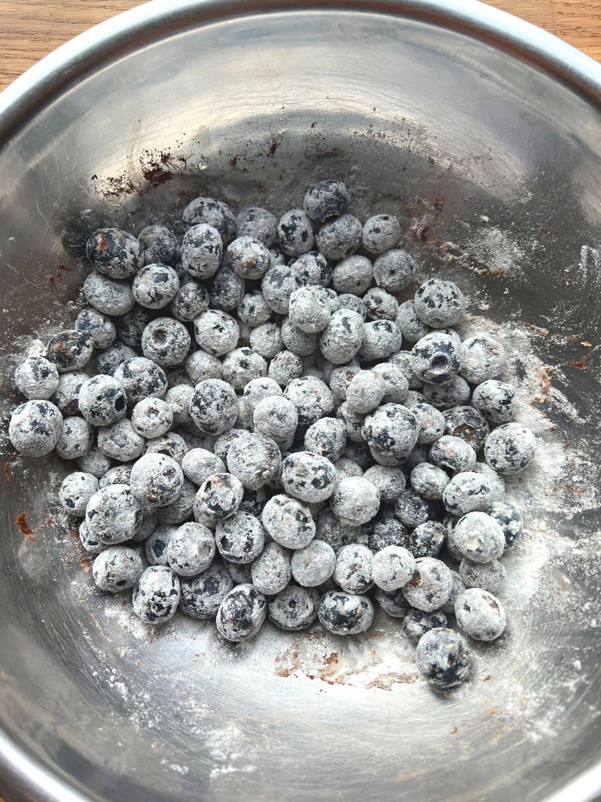 Blueberries tossed in flour and cinnamon in metal bowl.