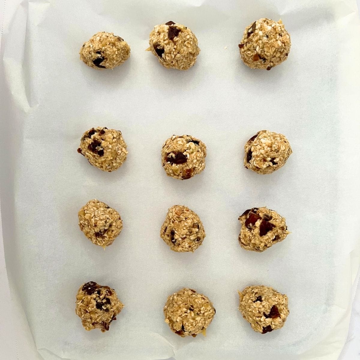 Cookie balls arranged on parchment paper on a  baking sheet.
