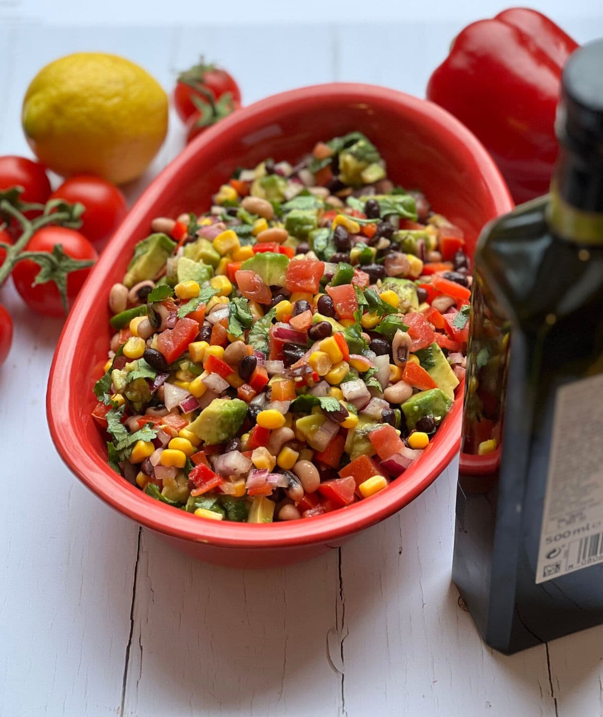 Cowboy salsa in red bowl surrounded by ingredients.