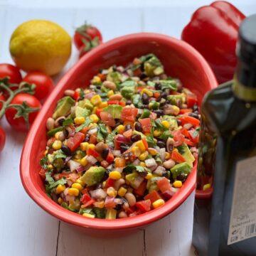 Cowboy salsa in a red bowl surrounded by ingredients.