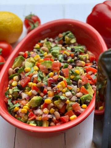 Cowboy salsa in a red bowl surrounded by ingredients.