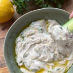 Closeup of tahini sauce with herbs in green bowl.