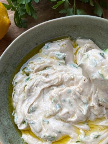 Closeup of tahini sauce with herbs in green bowl.