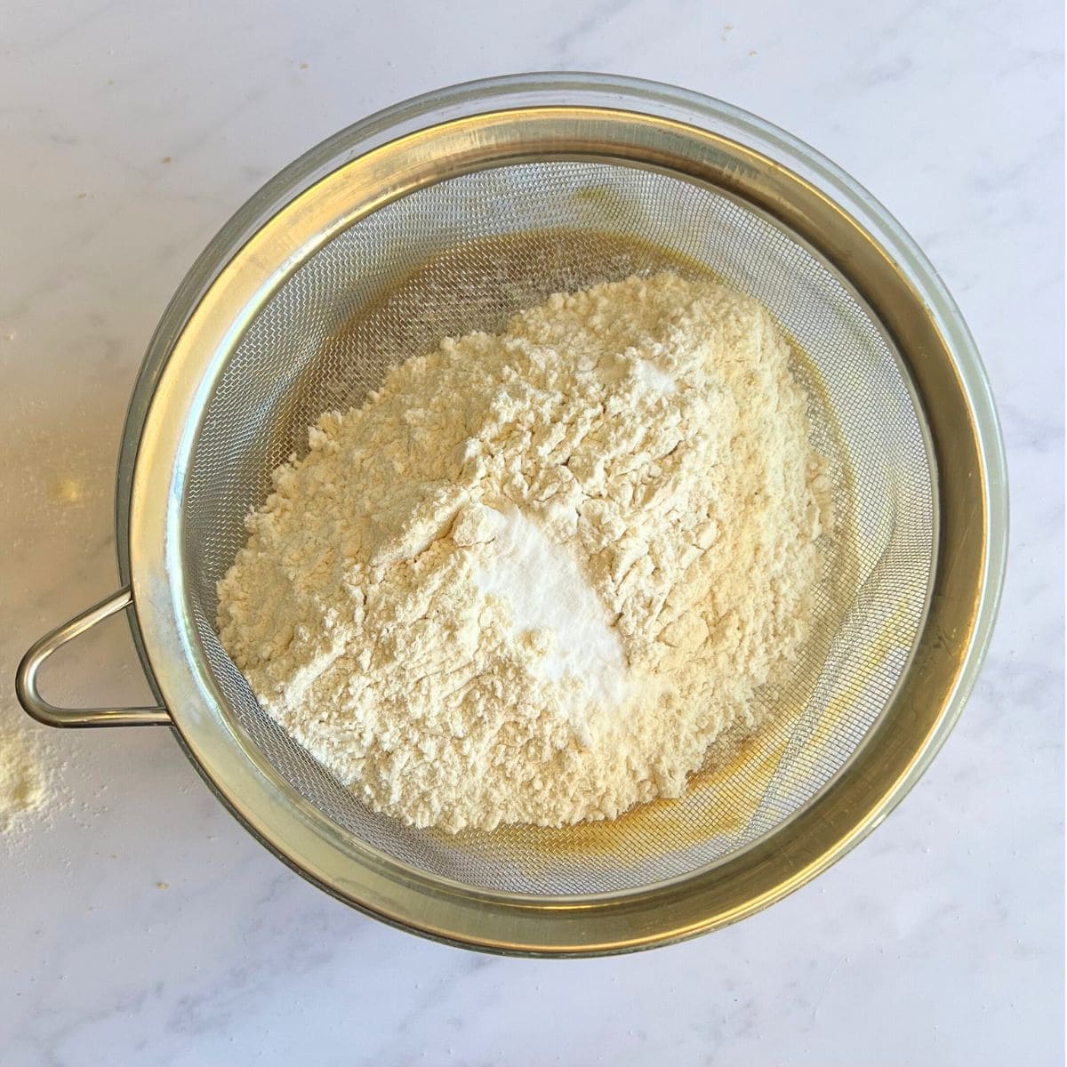 Sieve containing flour placed over bowl with cookie mixture.