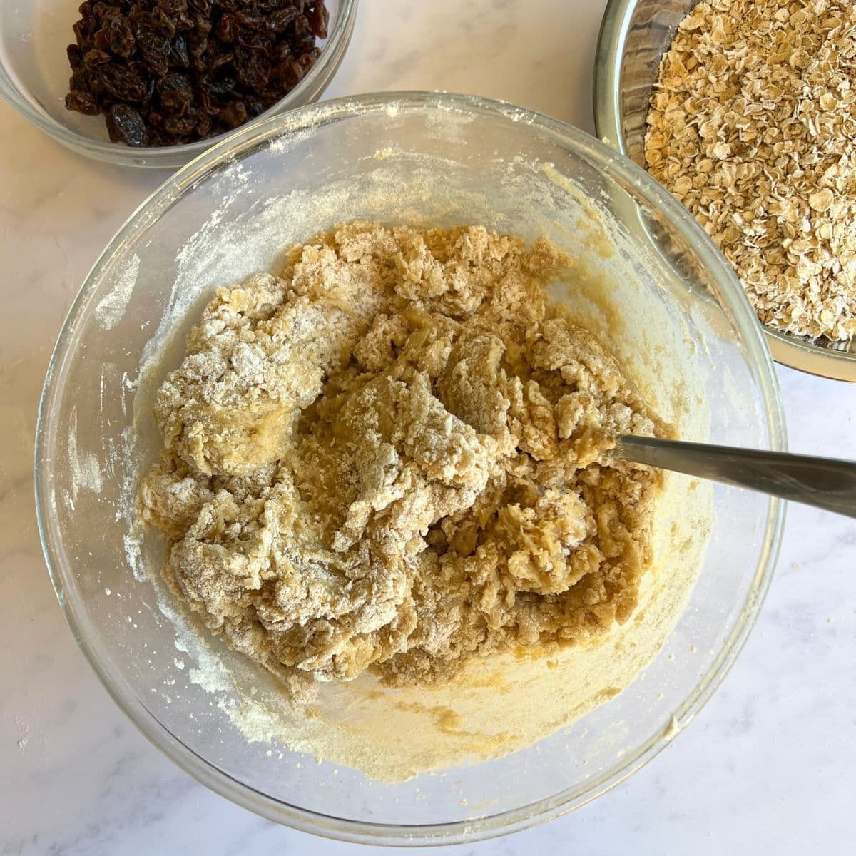 Mixture in bowl next to bowl of raisins and bowl of oats.