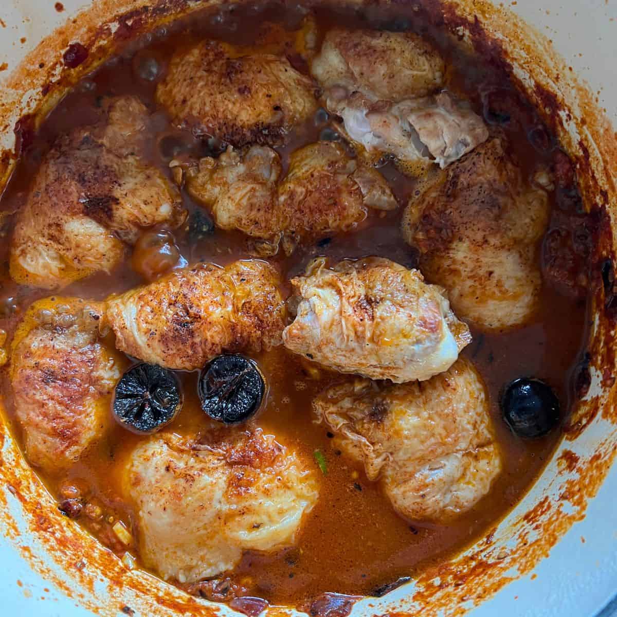 Chicken and dried limes cooking in sauce.
