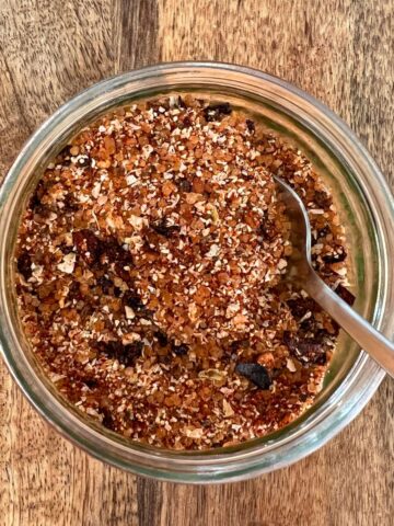 Chicken rub in small glass jar with spoon on wooden board.