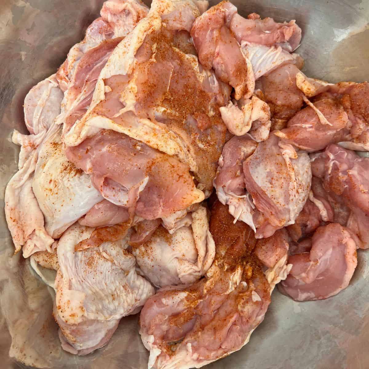 Raw chicken with dry rub in a metal bowl.