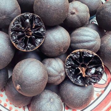 Dried black limes in bowl with one halved showing interior.