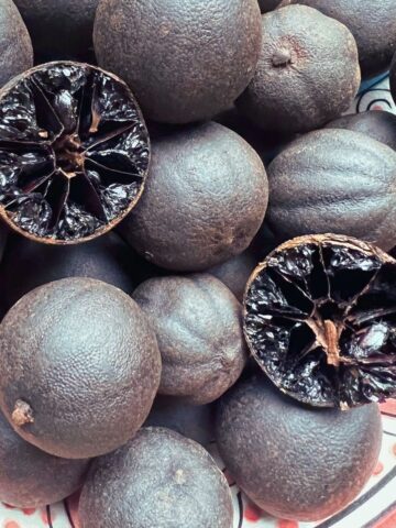 Dried black limes in bowl with one halved showing interior.