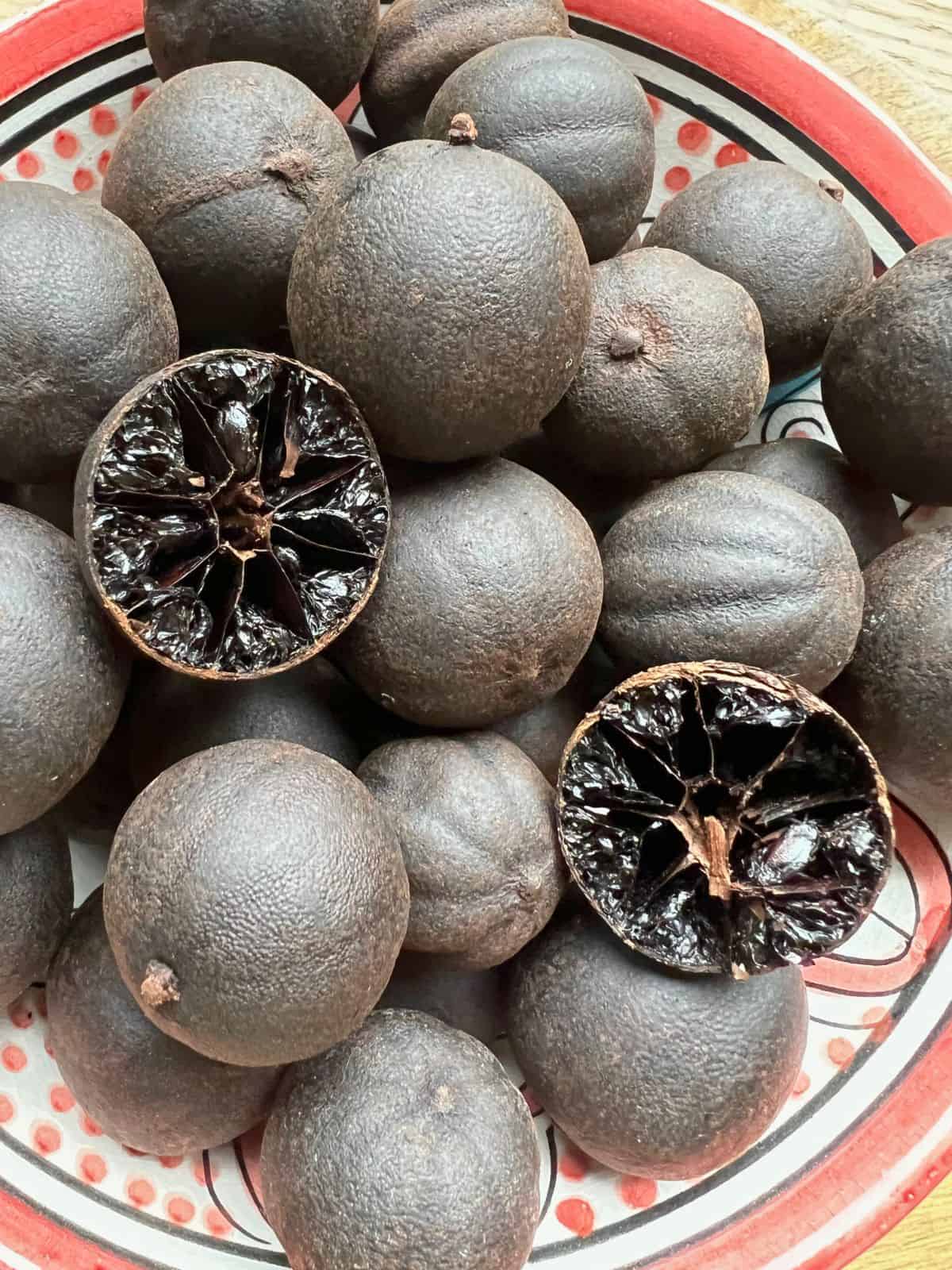Bowl full of dried black limes with one halved showing interior.