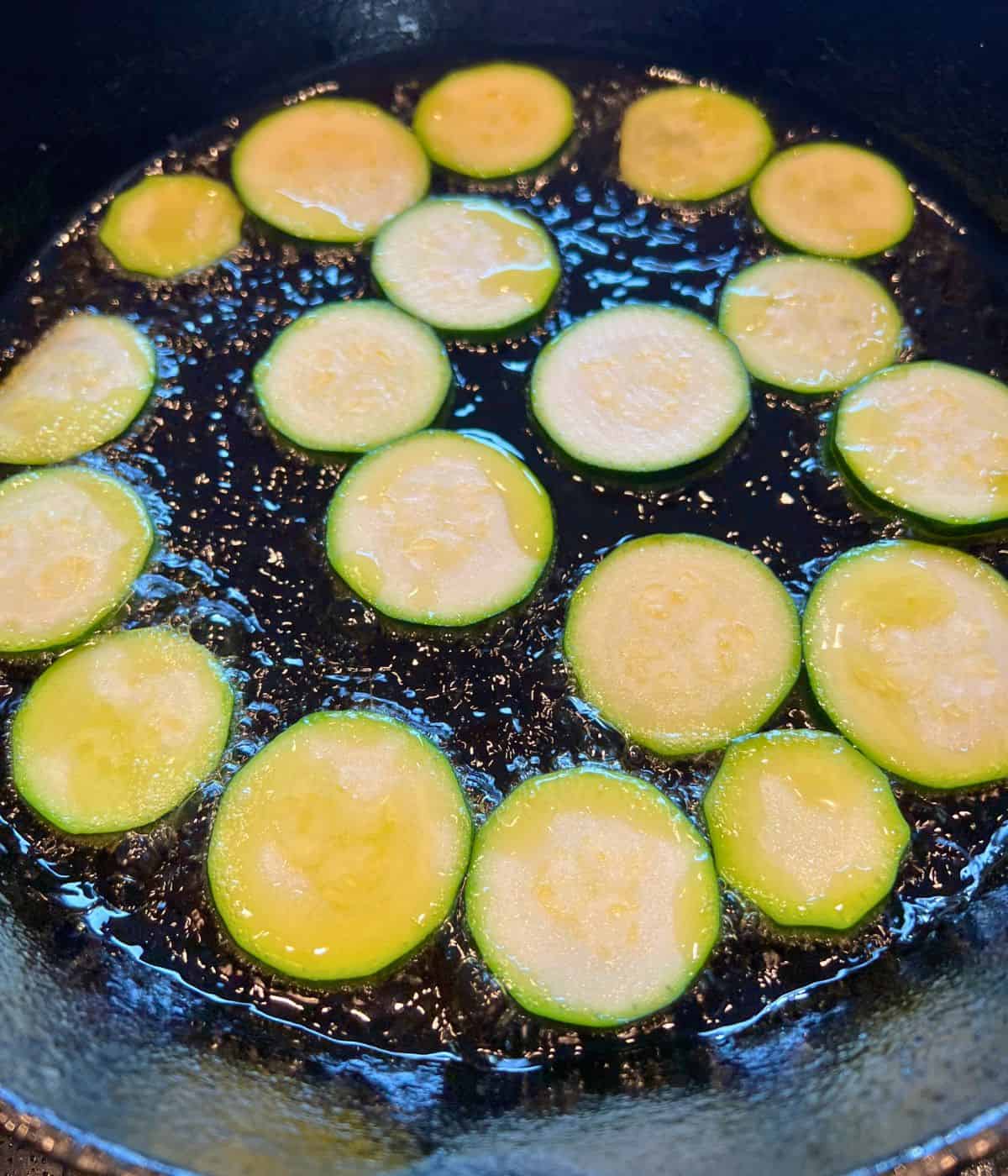 Shallow frying slices of zucchini in an iron skillet.