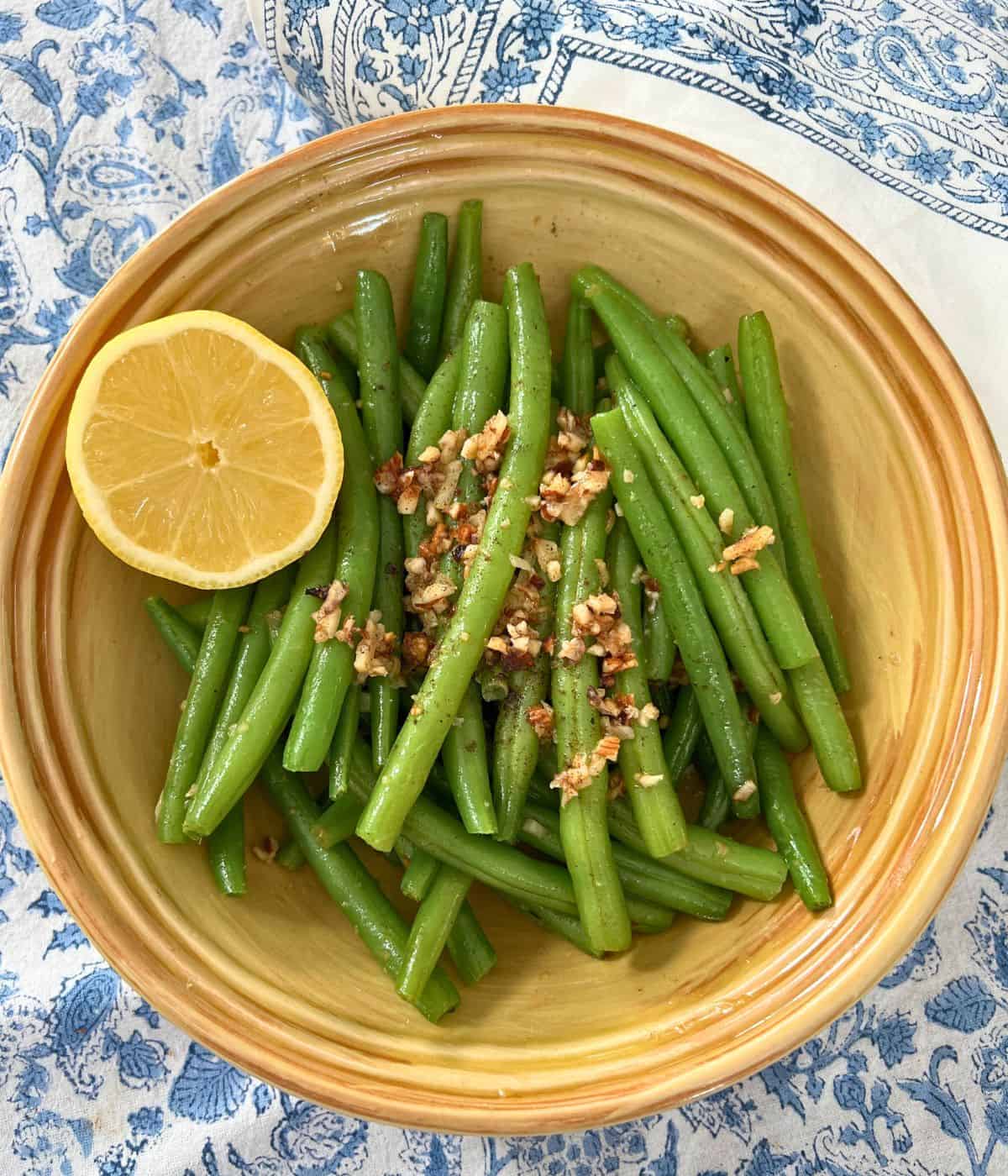 Sautéed green beans with garlic and lemon in a yellow bowl.