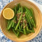 Green beans with roasted garlic and halved lemon in yellow bowl.