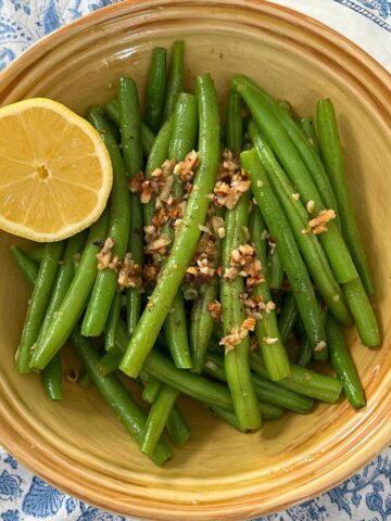 Green beans with roasted garlic and halved lemon in yellow bowl.