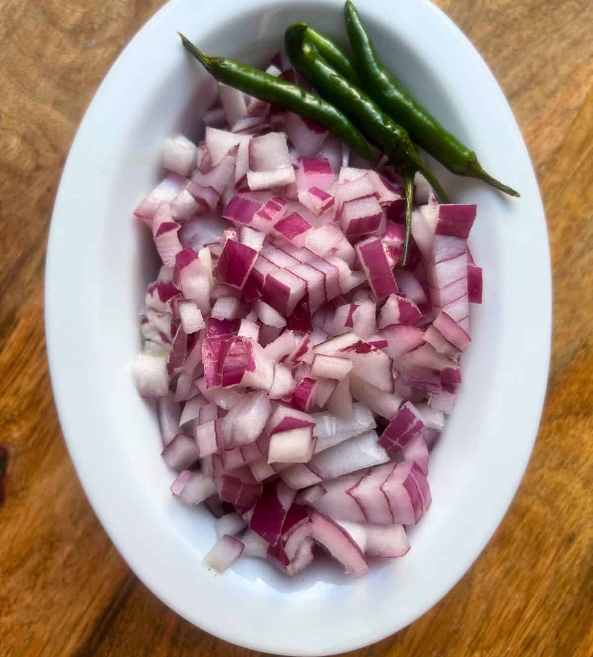 Chopped onion and whole green chillies in a small white bowl.