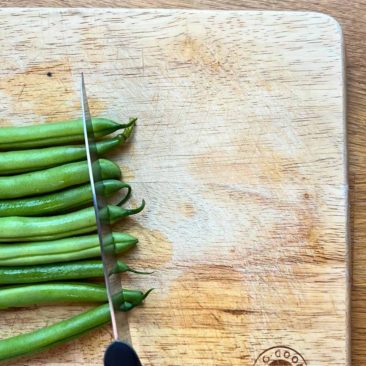 Trimming green beans on a chopping board.