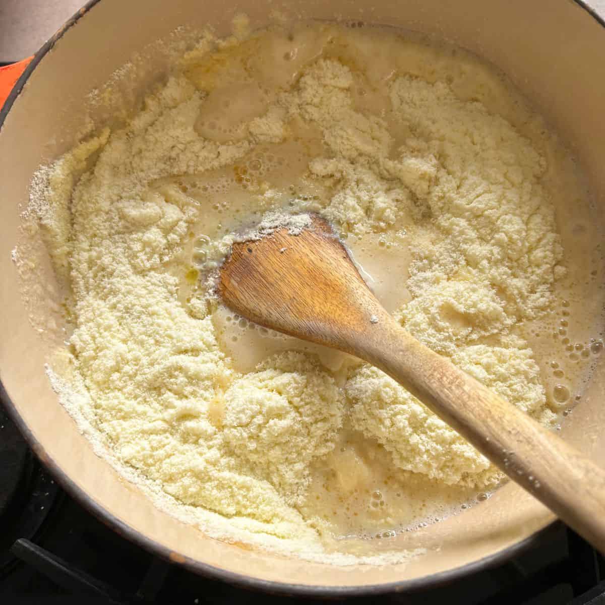 Wooden spoon stirring powdered milk into mixture in pan.