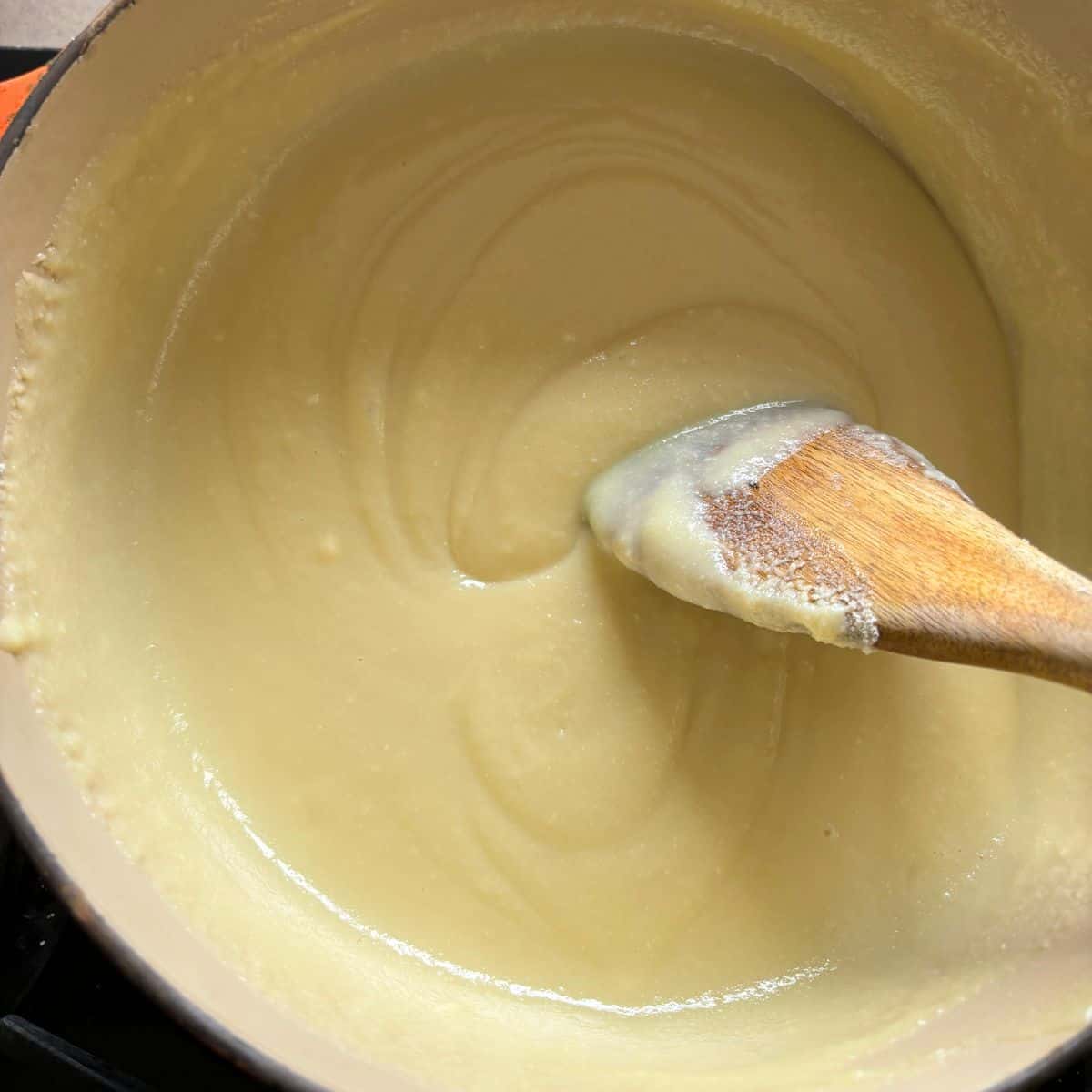 Wooden spoon stirring smooth mixture in pan.