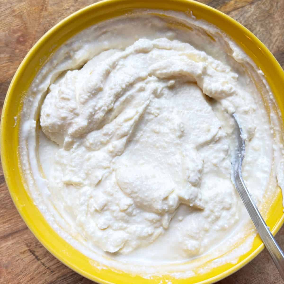 Cheese mixture in yellow bowl with spoon.