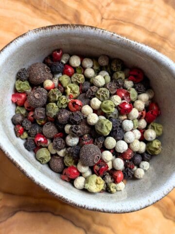 Black, white, green, red and pink peppercorns in a bowl.